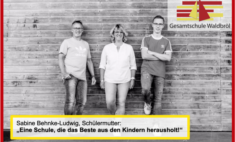 Drei Personen stehen vor einer Holzwand, mit einem Zitat zur Schule.