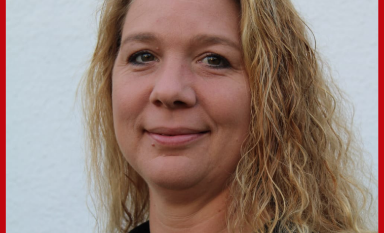 Porträt einer Frau mit kurzem, lockigem Haar vor einer weißen Wand.
