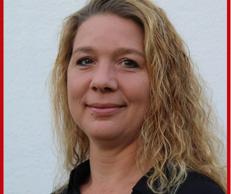 Porträt einer Frau mit kurzem, lockigem Haar vor einer weißen Wand.