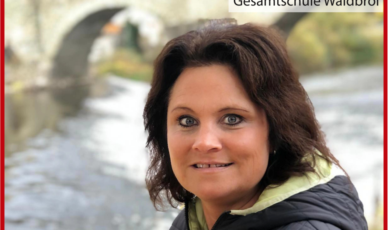 Frau mit dunklem Haar steht am Wasser, im Hintergrund eine Brücke.