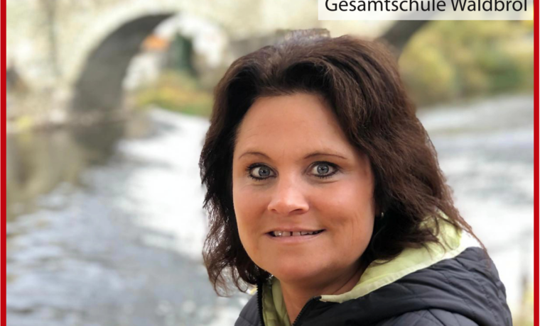 Frau mit dunklem Haar steht am Wasser, im Hintergrund eine Brücke.