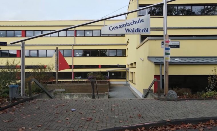Gesamtschule Waldiefeld, gelbes Gebäude mit Fahnen und Zugang über eine Rampe.