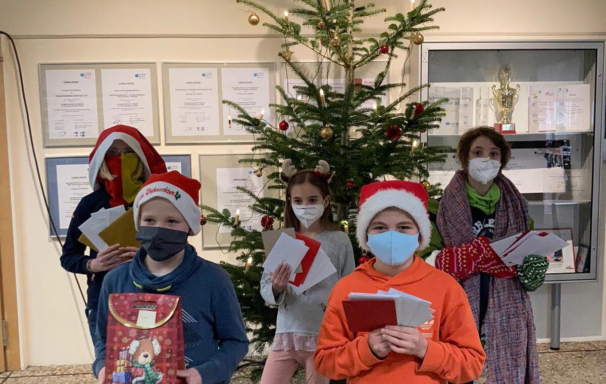 Gruppe von Kindern mit Weihnachtsmützen vor einem geschmückten Weihnachtsbaum.