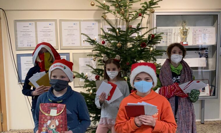 Gruppe von Kindern mit Weihnachtsmützen vor einem geschmückten Weihnachtsbaum.
