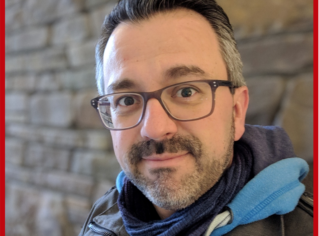 Porträt eines Mannes mit Brille und Schal vor einer Steinwand.