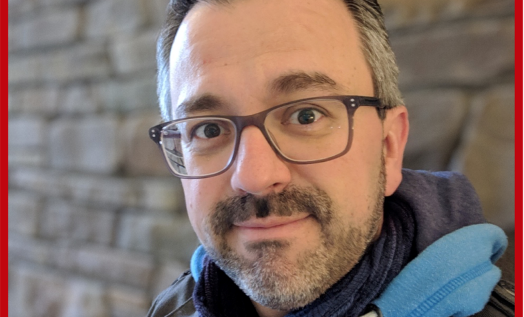 Porträt eines Mannes mit Brille und Schal vor einer Steinwand.