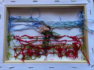 Buntes Fadenkunstwerk in einem Holzrahmen, mit verschiedenen Fäden angeordnet.