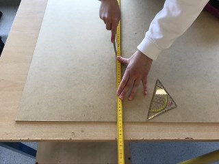 Eine Hand misst mit einem Zollstock auf einer Holzplatte.