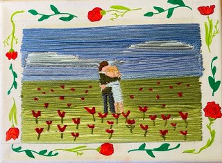 Ein Paar umarmt sich in einem blühenden Feld mit roten Blumen und blauem Himmel.