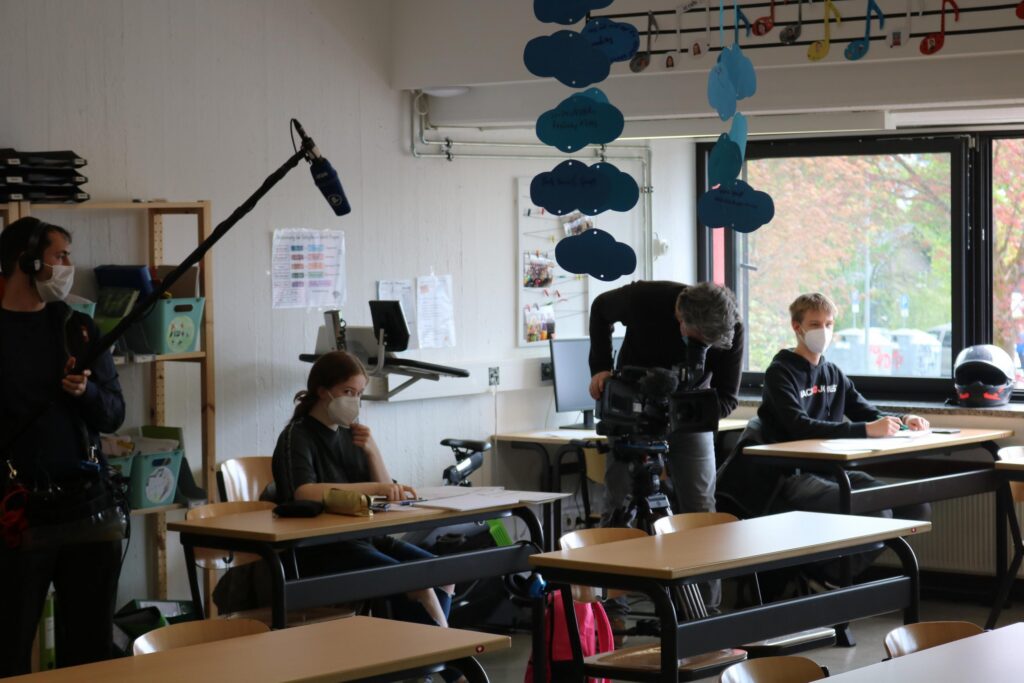 Schüler sitzen in einem Klassenzimmer, während Filmteam Aufnahmen macht.