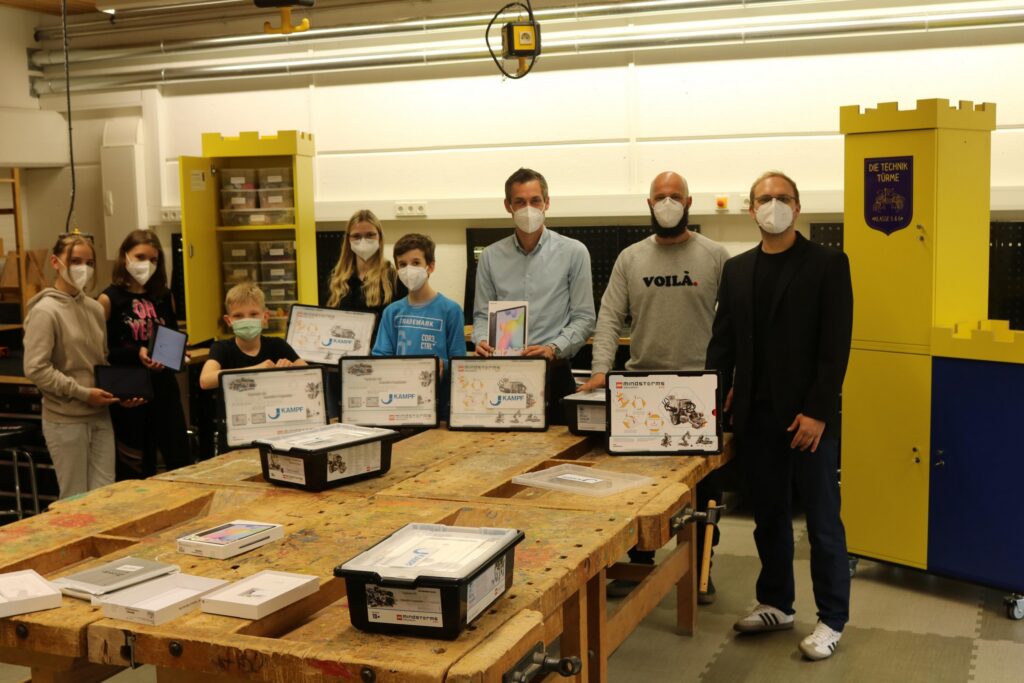 Gruppe von Personen mit Masken präsentiert Projekte in einem Werkraum.