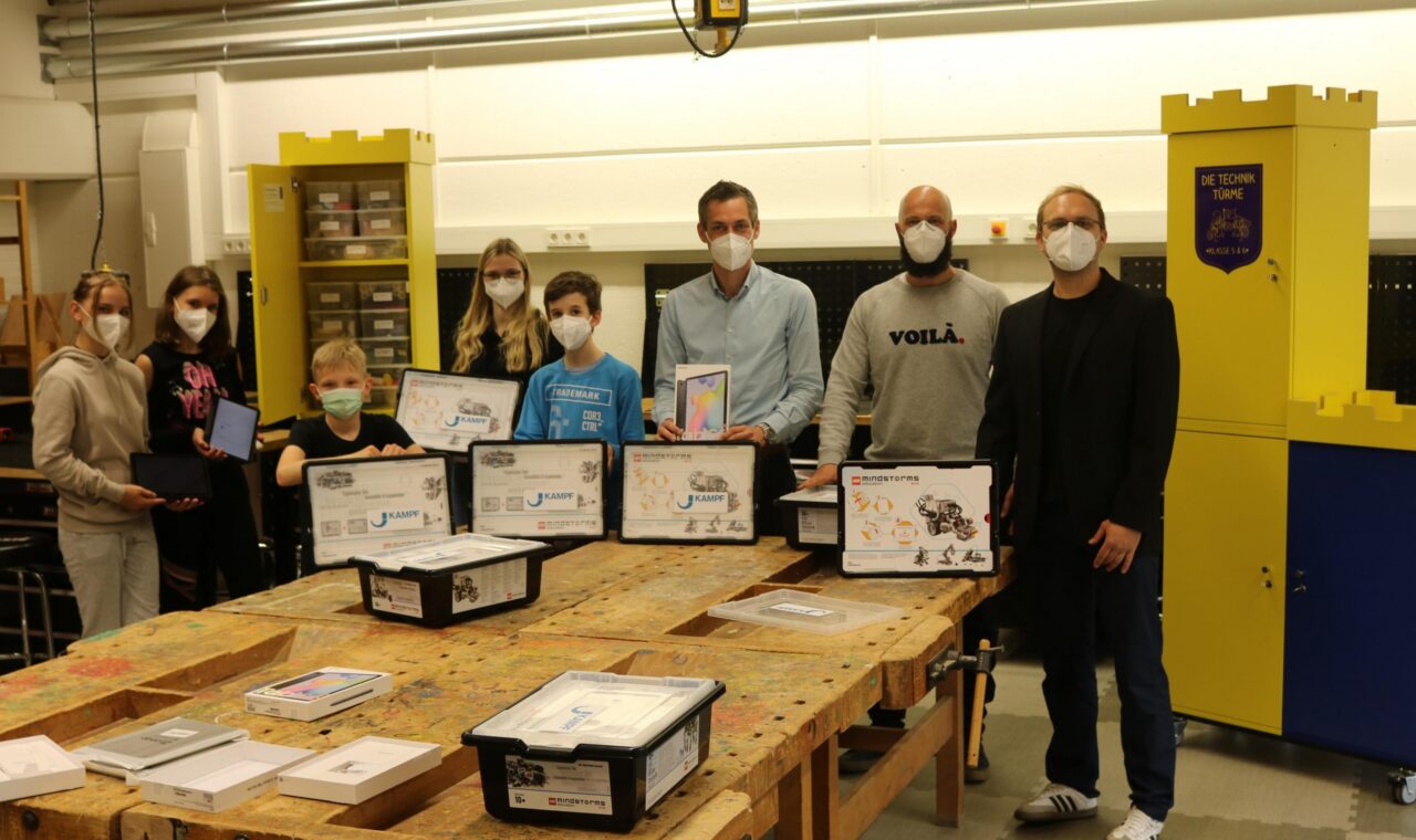 Gruppe von Personen mit Masken präsentiert Projekte in einem Werkraum.