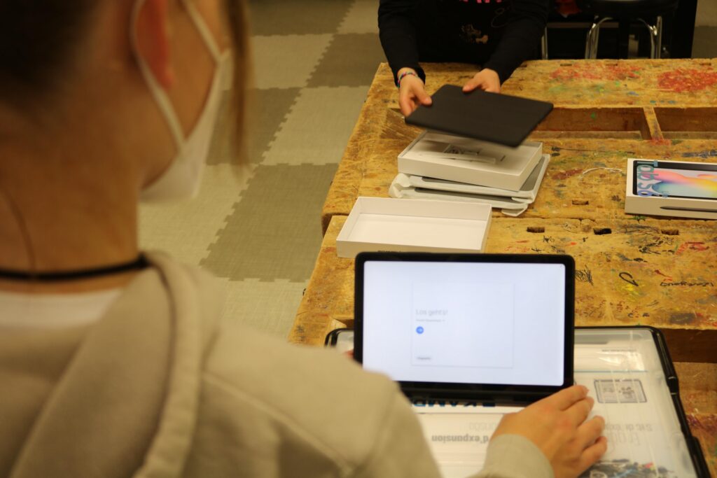 Schülerin arbeitet an Laptop, während eine andere Person ein Tablet hält.