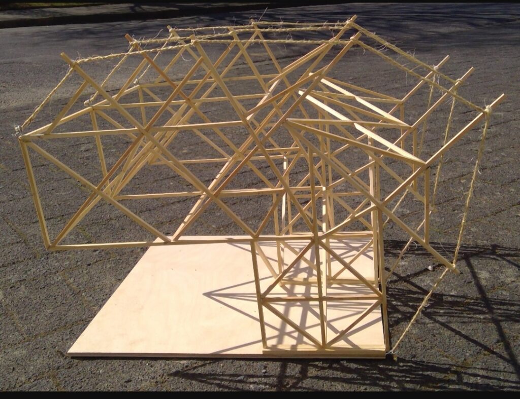 Modell aus Holzstäben in geometrischer Struktur auf einer Holzplatte.