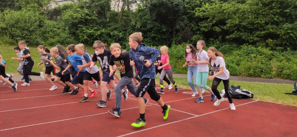 Kinder laufen auf einer Laufbahn, einige starten einen Wettlauf.