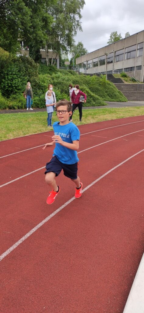 Schüler läuft schnell auf einer Laufbahn, im Hintergrund stehen andere Schüler.