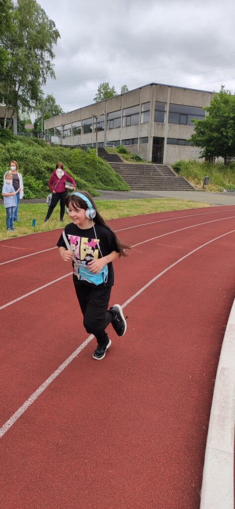 Ein Mädchen läuft auf einer Laufbahn, im Hintergrund ein Schulgebäude.