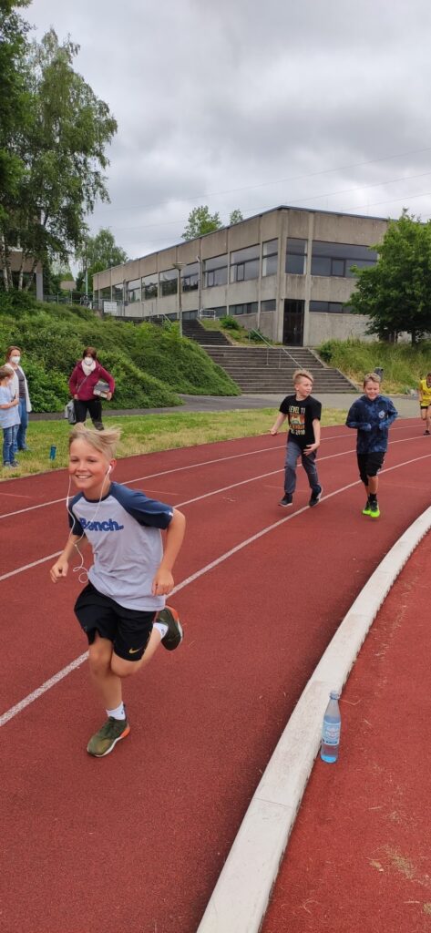 Kinder laufen auf einer Laufbahn, im Hintergrund ein Schulgebäude.