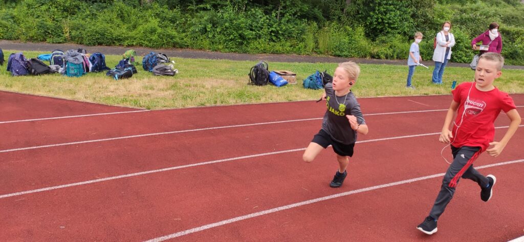 Zwei Jungen sprinten auf einer Laufbahn, im Hintergrund stehen einige Zuschauer.