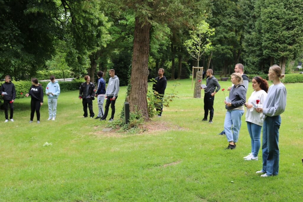 Gruppe von Schülern steht auf einer Wiese neben einem Baum.