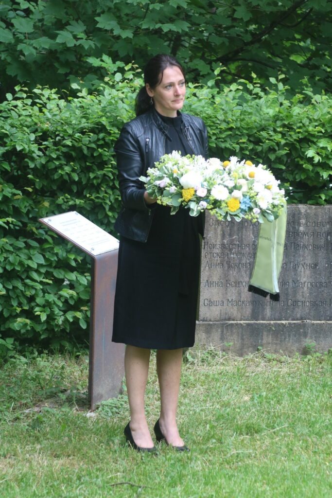 Frau hält einen Blumenstrauß in einer Gedenkstätte.