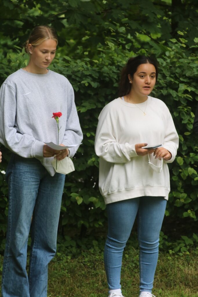 Zwei Schülerinnen stehen im Freien und halten Blumen und Zettel in der Hand.