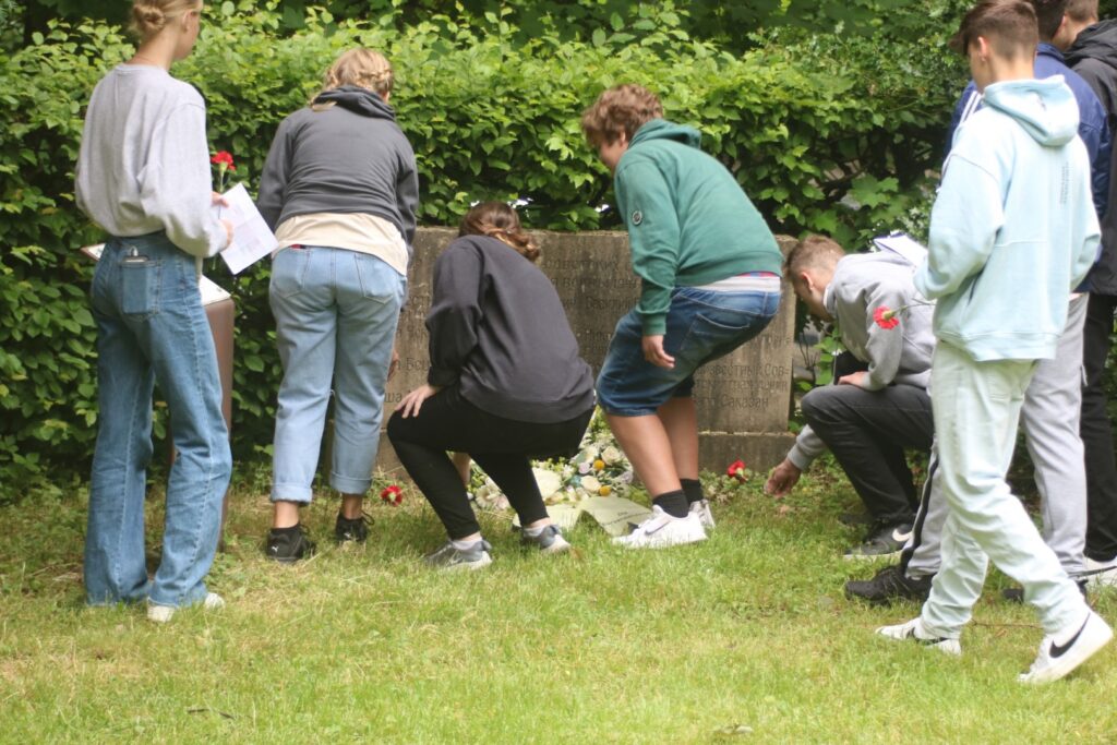 Schüler pflücken Blumen und legen sie an einem Gedenkstein nieder.