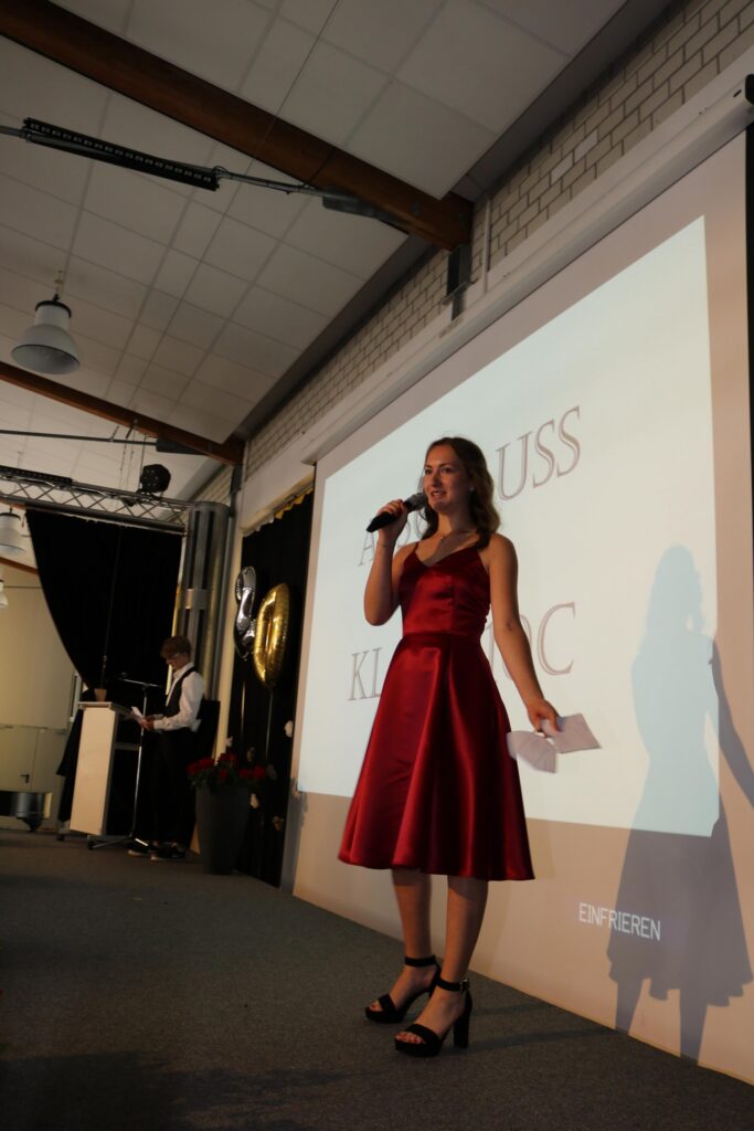 Ein Mädchen in einem roten Kleid steht mit einem Mikrofon auf einer Bühne.