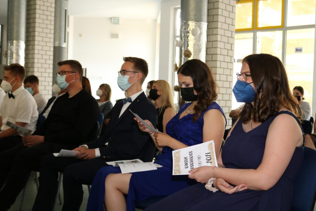 Gruppe von Schülern in eleganter Kleidung bei einer Veranstaltung, alle tragen Masken.