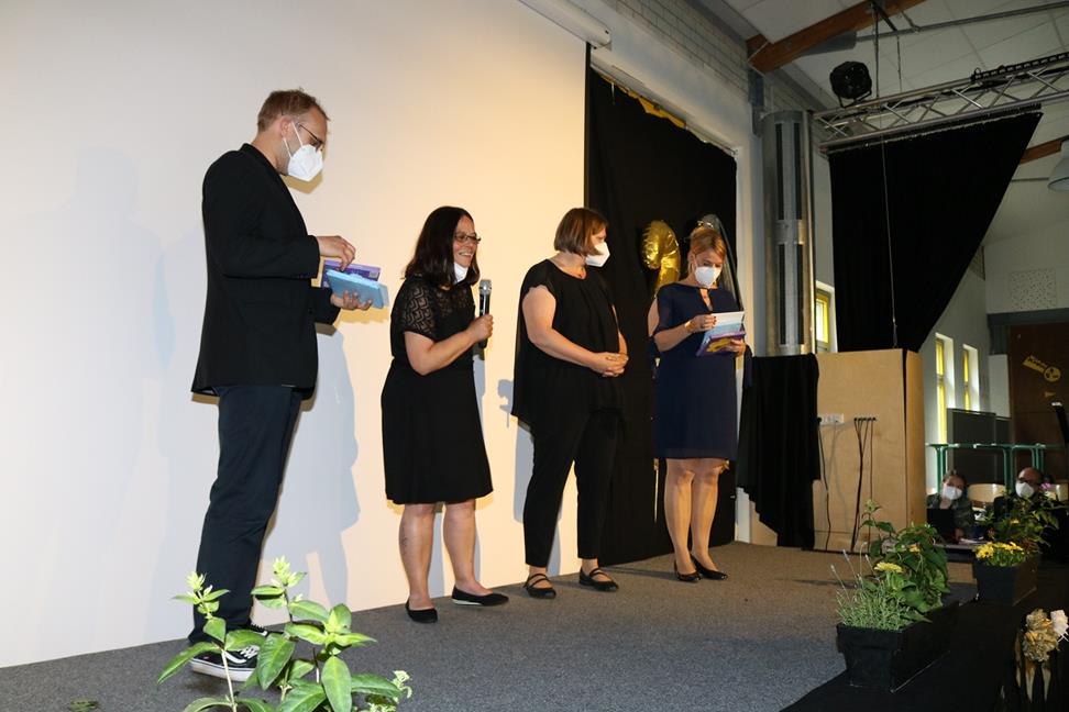 Vier Personen stehen auf einer Bühne und sprechen ins Mikrofon.