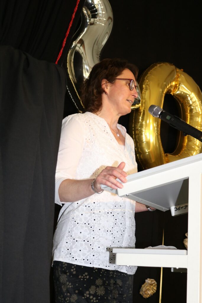 Eine Frau steht an einem Rednerpult und spricht in ein Mikrofon.