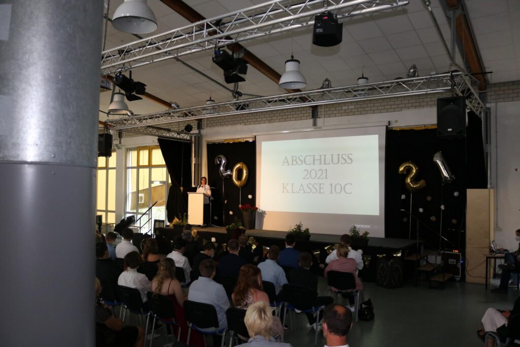 Blick auf eine Aula mit Publikum und Präsentationsleinwand.