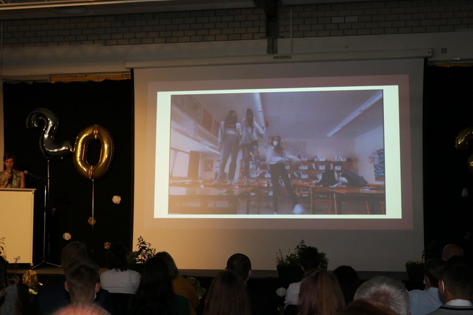 Präsentation auf großer Leinwand mit Feierlichkeiten im Hintergrund.