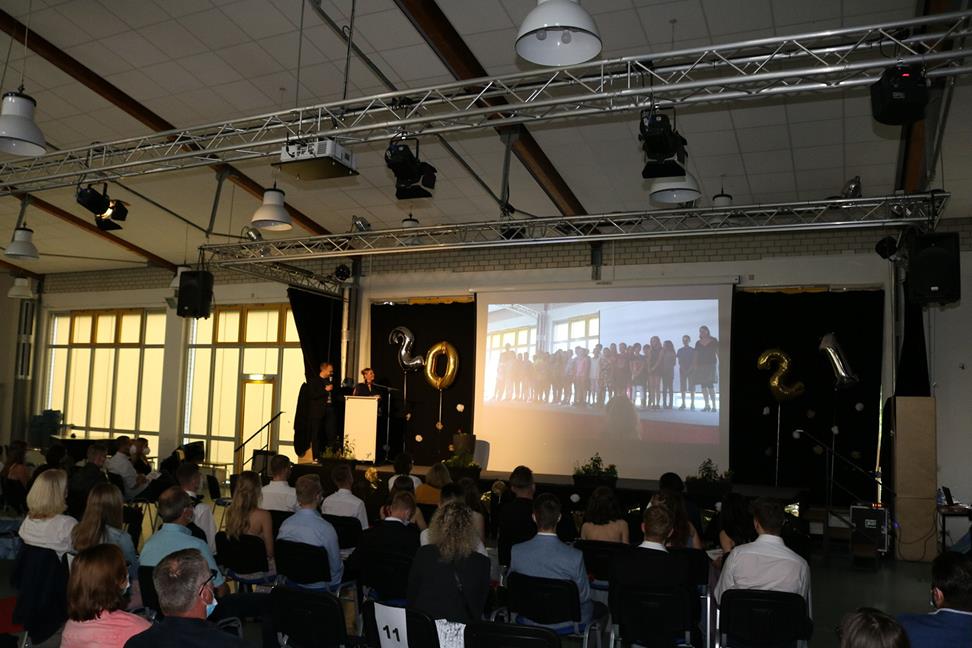 Feierliche Veranstaltung mit Publikum und Präsentation auf großer Leinwand.