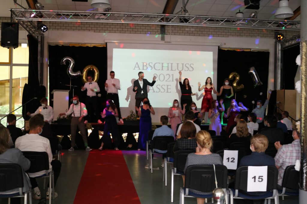 Schülerinnen und Schüler tanzen auf einer Abschlussparty vor einer Leinwand.