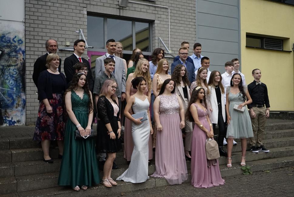 Gruppe von Schülern in festlicher Kleidung vor einem Gebäude.