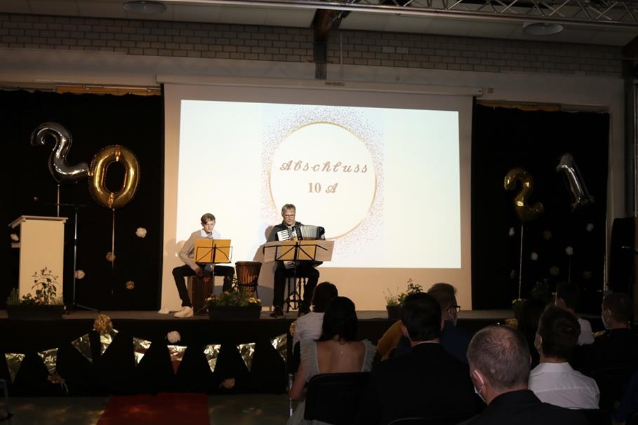Zwei Musiker spielen auf der Bühne vor einer Projektion und Publikum.