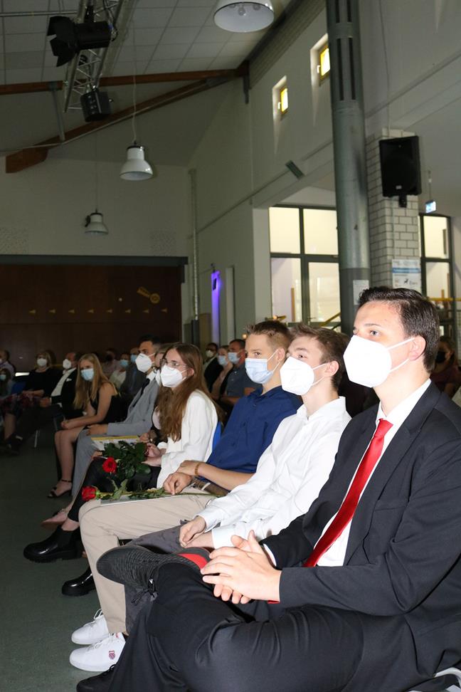 Schüler und Lehrer sitzen während einer Veranstaltung, alle tragen Masken.
