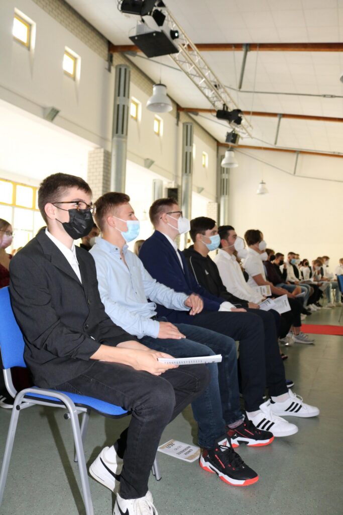 Schüler in Reihen sitzen während einer Veranstaltung in einem Saal.