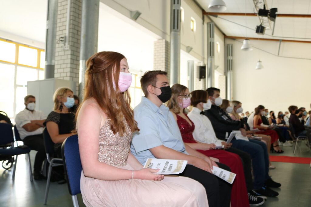 Schülerinnen und Schüler sitzen in Reihen bei einer Veranstaltung und tragen Masken.