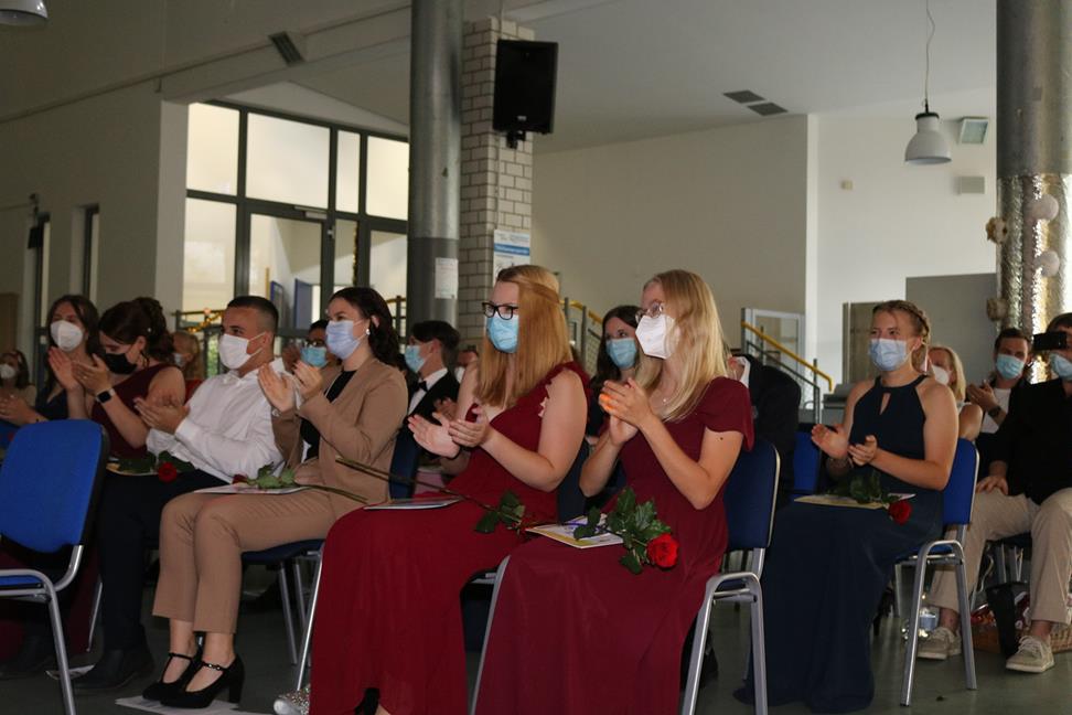 Schülerinnen und Schüler sitzen in einem Saal, applaudieren und tragen Schutzmasken.