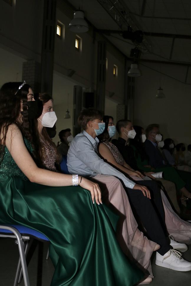 Gruppe von Jugendlichen in eleganter Kleidung, sitzen mit Mund-Nasen-Schutz.
