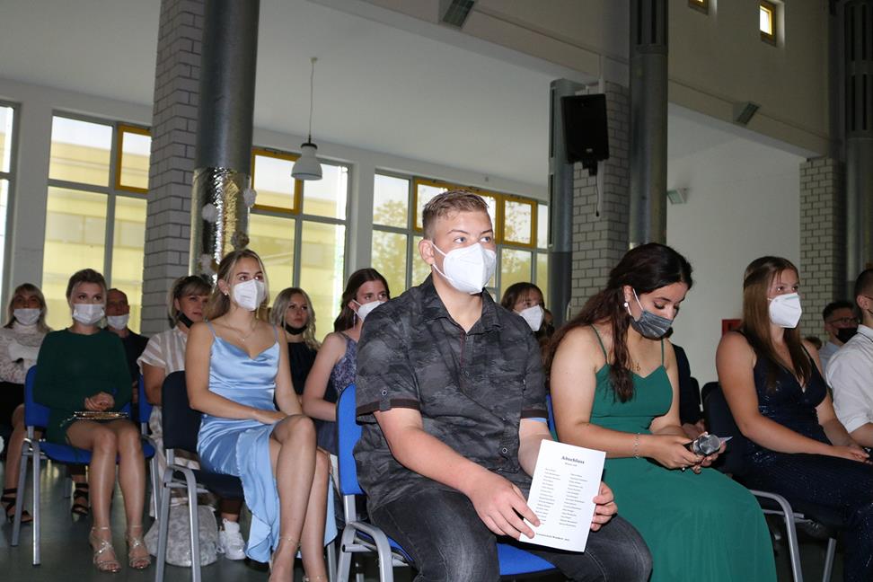 Schülerinnen und Schüler in Masken sitzen bei einer Veranstaltung im Saal.
