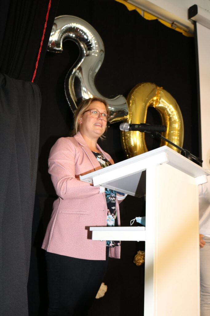 Frau am Rednerpult vor goldenen Luftballons mit der Zahl 20.
