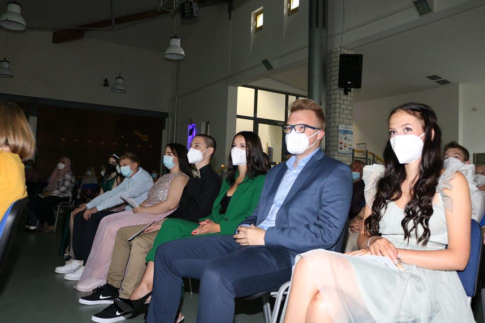 Schüler und Lehrkräfte sitzen in einem Saal mit Masken während einer Veranstaltung.