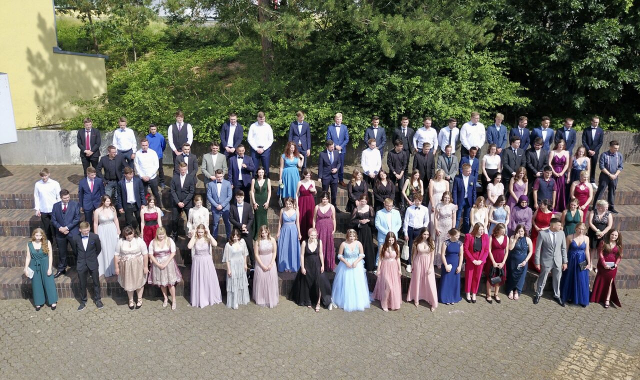 Gruppe von Absolventen in Abendkleidung auf einer Treppe im Freien.