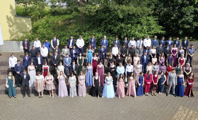 Gruppe von Absolventen in Abendkleidung auf einer Treppe im Freien.