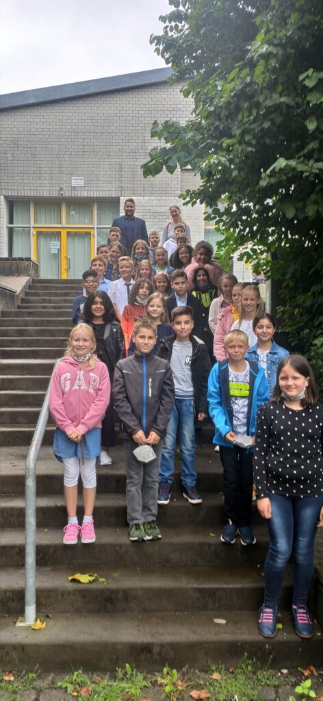 Gruppe von Schülern und Lehrern posiert auf einer Treppe vor einem Schulgebäude.