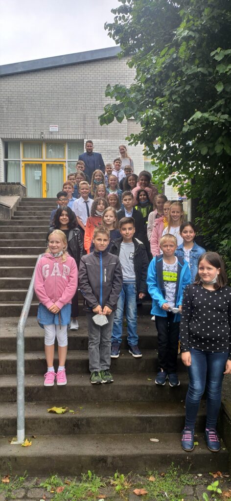Schülergruppe steht lächelnd auf Treppen vor einem Schulgebäude.