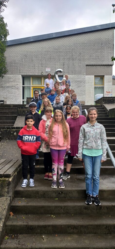 Gruppe von Schülerinnen und Schülern steht auf Treppen vor einem Schulgebäude.